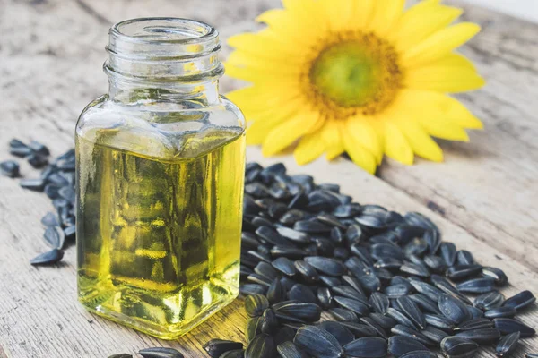 Aceite de girasol en un frasco de vidrio con semillas y flores frescas sobre un fondo de madera. Alimentos y grasas saludables . — Foto de Stock