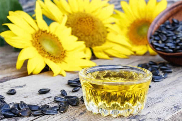 Sunflower oil and sunflower seeds in a bowl on a wooden background near fresh sunflower flowers. Organic and eco food. — Stock Photo, Image