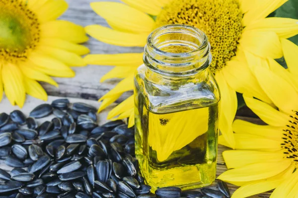 Bio slunečnicový olej ve skleněné nádobě se semeny a čerstvými květy na dřevěném podkladu. Zdravé potraviny a tuky. — Stock fotografie