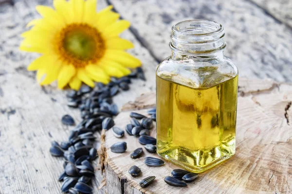 Aceite de girasol orgánico en un frasco de vidrio con semillas y flores frescas sobre un fondo de madera. Alimentos y grasas saludables . — Foto de Stock