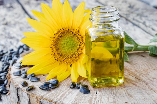 Girasoles y semillas sobre un fondo de madera cerca del aceite de girasol en un frasco de vidrio. Alimentos y grasas saludables . — Foto de Stock