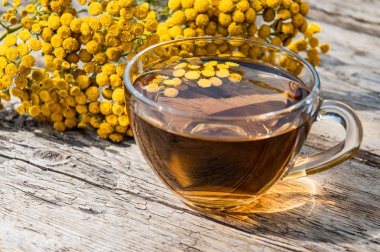 Ahşap bir masa üzerinde sarı tansy çiçekleri yakınında tansy şifalı otlar ile çay Fincan. Şifa otlar.