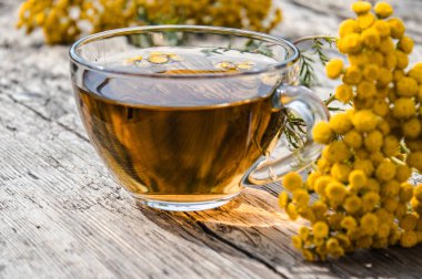 Ahşap bir masa üzerinde tansy ve tansy çiçekleri ile çay fincan. Şifa otlar.