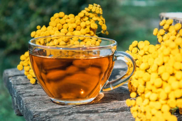 Tansy infusion in a glass cup on a wooden table. Tansy Herbal tea. Healing herbs. — Stock Photo, Image
