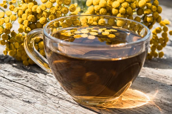 Ahşap bir masa üzerinde tansy ve tansy çiçekleri ile çay fincan. Şifa otlar.