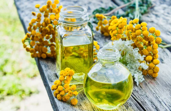 Tansy essential oil in a glass bottle on a wooden background near yellow tansy flowers. Tincture extract with medicinal tansy. Herbal medicine concept. — Stock Photo, Image