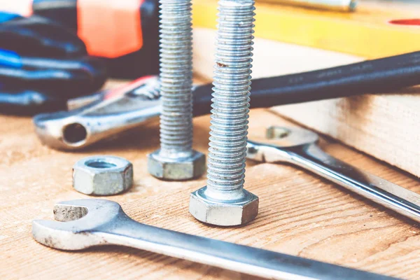 Çelik cıvata somunları ve yıkıtaları ayarlanabilir bir anahtar ve bant ölçüsü yakınında ahşap tahtalar üzerinde yalan.