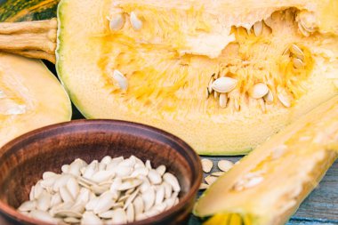 Mavi eski tahtalarda olgun bir kabak yakın bir kase içinde kabak tohumları.