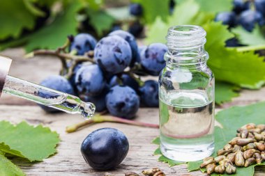 Cam bir kavanozda üzüm çekirdeği yağı ve eski ahşap tahtalar üzerinde taze üzüm. Spa, Eko ürünler konsepti.