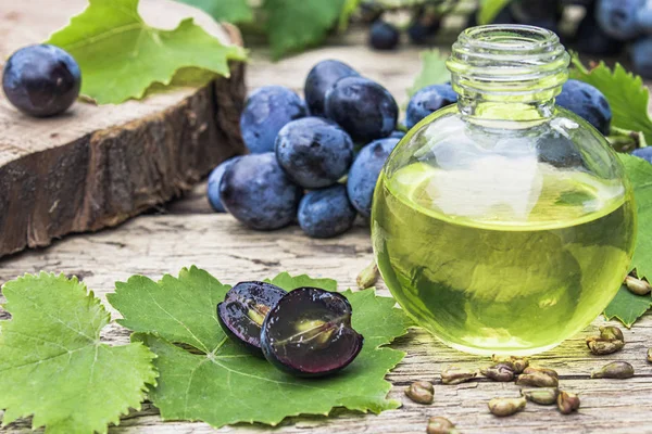 Szőlőmag olaj egy üvegpalack közelében kék szőlő és a zöld levelek a régi fa deszkák. Spa, öko termékek koncepció. — Stock Fotó