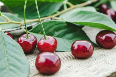 Ahşap masada yeşil yaprakları ile kırmızı kiraz ve dalları.