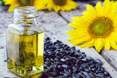 Ahşap bir arka plan üzerinde tohum ve taze çiçekler ile cam bir kavanozda ayçiçek yağı. Sağlıklı gıdalar ve yağlar.