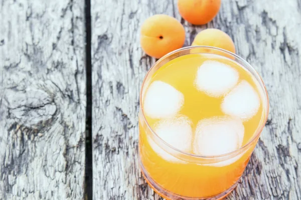 Fresh apricot juice with apricots and ice cubes in a glass against the background of old boards. Summer soft drinks.