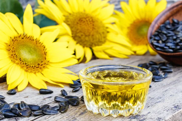 Sunflower oil and sunflower seeds in a bowl on a wooden background near fresh sunflower flowers. Organic and eco food. — Stock Photo, Image