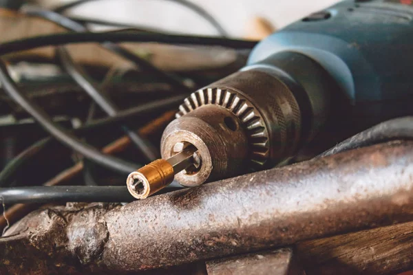 An electric drill lies on a pile of cable and hammers.