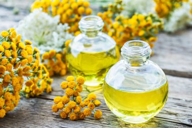 Sarı tansy çiçekler yakınında ahşap bir arka plan üzerinde bir cam şişe tabakesi uçucu yağ. Tıbbi tansy ile tentür özü. Bitkisel ilaç kavramı.