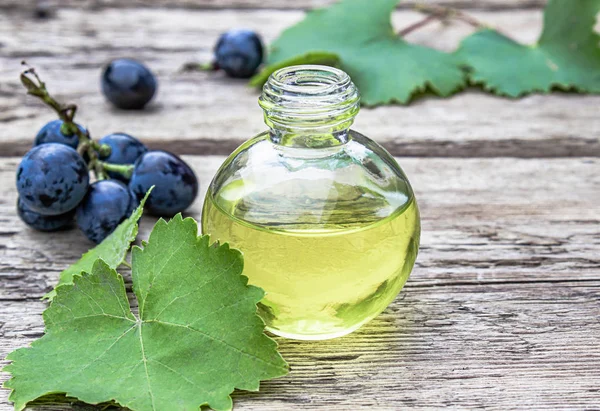 Aceite de semilla de uva en una botella de vidrio cerca de uvas azules y hojas verdes en viejas tablas de madera. Spa, concepto de productos ecológicos . — Foto de Stock