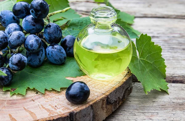 Aceite de semilla de uva en una botella de vidrio cerca de uvas azules y hojas verdes en viejas tablas de madera. Spa, concepto de productos ecológicos . — Foto de Stock