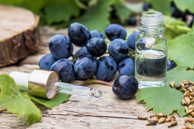 Cam bir kavanozda üzüm çekirdeği yağı ve eski ahşap tahtalar üzerinde taze üzüm. Spa, Eko ürünler konsepti.