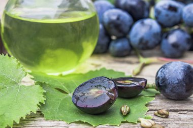 Eski ahşap tahtalar üzerinde mavi üzüm ve yeşil yaprakları yakınında bir cam şişe üzüm çekirdeği yağı. Spa, eko ürünler konsepti.