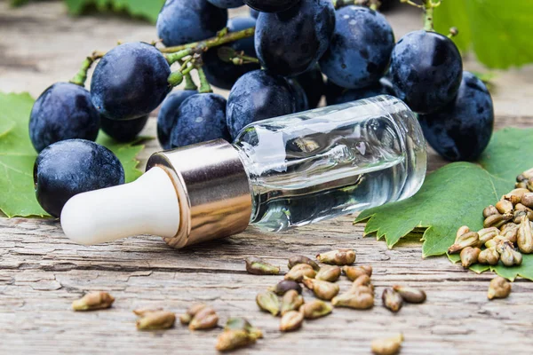 Palack szőlőmag illóolaj a régi fa táblák közelében Grones kék szőlő és zöld levelek. Spa, öko termékek koncepció. — Stock Fotó