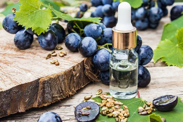 Бутылка с виноградным семенем эфирного масла на старых деревянных досках рядом с решетками из голубого винограда и зеленых листьев. Spa,,, eco products concept . — стоковое фото