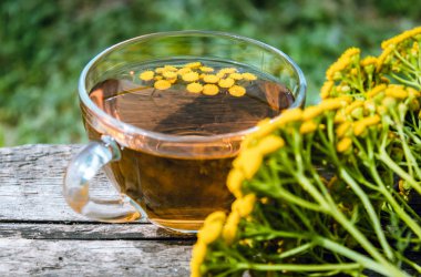 Doğanın arka planına karşı ahşap bir masanın yüzeyinde bir kupa ve sarı tansy çiçekler bitkisel çay veya tansi tentür. Şifa otlar.