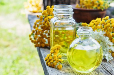 Sarı tansy çiçekler yakınında ahşap bir arka plan üzerinde bir cam şişe tabakesi uçucu yağ. Tıbbi tansy ile tentür özü. Bitkisel ilaç kavramı.