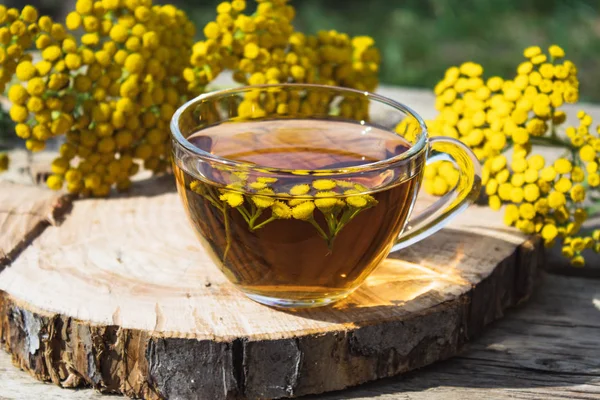 Настой Тензи в стеклянной чашке и желтые нежные цветы на деревянном столе. Тензи Травяной чай. Лечебные травы . — стоковое фото