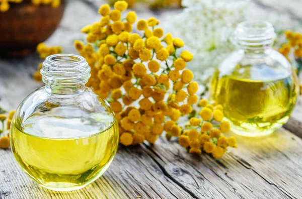 Eski bir ahşap arka plan üzerinde sarı tansy yakın bir cam şişe tabakesi uçucu yağ. Bitkisel ilaç kavramı.