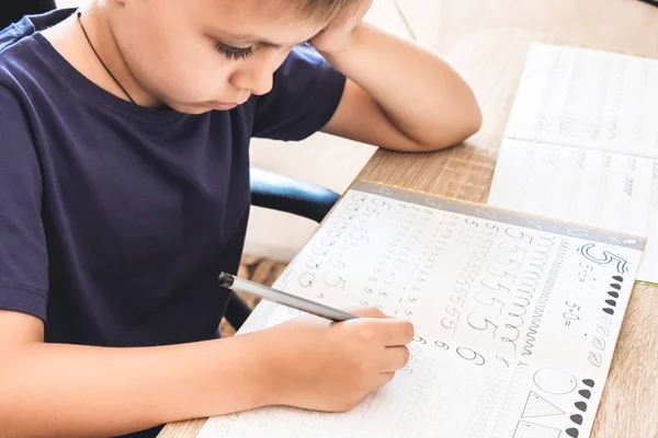 Een school jongen leert schrijven in een notebook. Potlood in de handen van kinderen. — Stockfoto