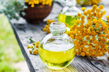 Eski bir ahşap arka plan üzerinde sarı tansy yakın bir cam şişe tabakesi uçucu yağ. Bitkisel ilaç kavramı.