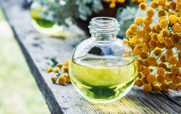 Eski bir ahşap arka plan üzerinde sarı tansy yakın bir cam şişe tabakesi uçucu yağ. Bitkisel ilaç kavramı.