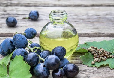 Eski ahşap tahtalar üzerinde mavi üzüm ve yeşil yaprakları yakınında bir cam şişe üzüm çekirdeği yağı. Spa, eko ürünler konsepti.