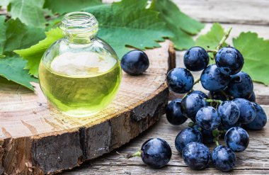 Eski ahşap tahtalar üzerinde mavi üzüm ve yeşil yaprakları yakınında bir cam şişe üzüm çekirdeği yağı. Spa, eko ürünler konsepti.
