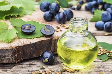 Cam bir kavanozda üzüm çekirdeği yağı ve eski ahşap tahtalar üzerinde taze üzüm. Spa, Eko ürünler konsepti.