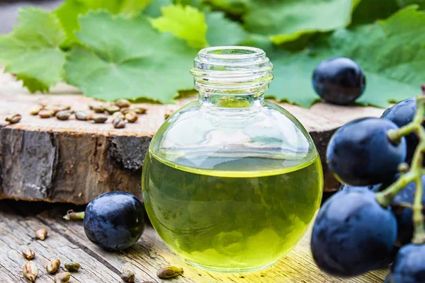 Bir cam şişe üzüm uçucu yağ ve eski ahşap tahtalar üzerinde zar. Mavi üzüm. Spa, eko ürünler konsepti.