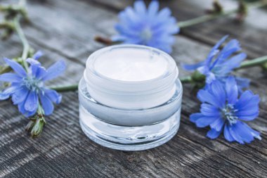 Eski bir ahşap masa üzerinde cam bir kavanozda mavi hindiba çiçek ve yüz kremi. Sağlık kavramı.