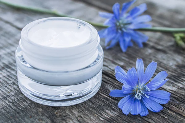 Flor de achicoria azul y crema facial en un frasco de vidrio sobre una vieja mesa de madera. Concepto de salud . — Foto de Stock