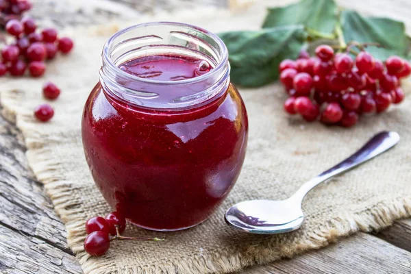 Olgun kırmızı viburnum meyveleri yakınında ahşap bir masa üzerinde bir cam kavanozda Viburnum meyve reçeli. Doğal vitaminlerin kaynağı. Halk hekimliğinde kullanılır.