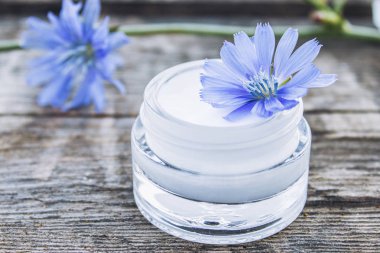 Eski bir ahşap masa üzerinde cam bir kavanozda mavi hindiba çiçek ve yüz kremi. Sağlık kavramı.