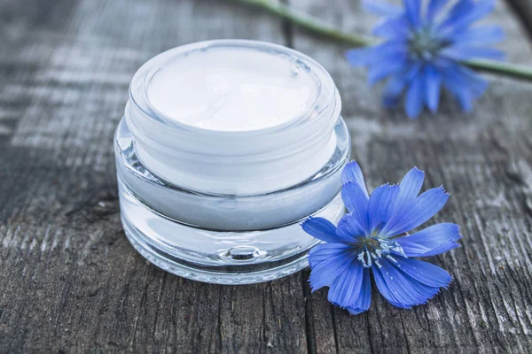 Flor de achicoria azul y crema facial en un frasco de vidrio sobre una vieja mesa de madera. Concepto de salud . — Foto de Stock