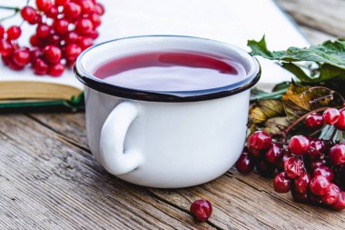 Açık bir kitap ve kırmızı viburnum çilek yakınında ahşap bir masada beyaz kupa veya sıcak viburnum çay fincan. Doğal vitaminlerin kaynağı. Halk hekimliğinde kullanılır.