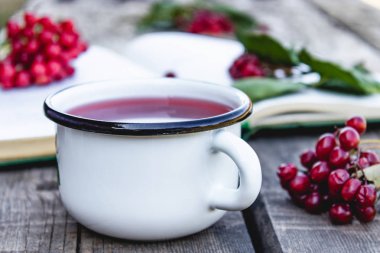 Açık bir kitap ve kırmızı viburnum çilek yakınında ahşap bir masada beyaz kupa veya sıcak viburnum çay fincan. Doğal vitaminlerin kaynağı. Halk hekimliğinde kullanılır.