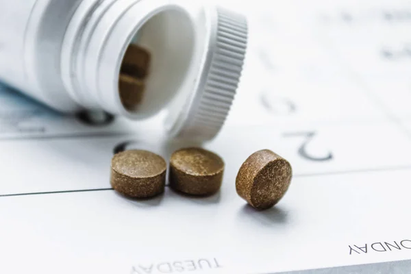 Petites pilules sombres à côté d'un pot blanc ou une bouteille sur un fond de calendrier. Le remède contre la maladie . — Photo