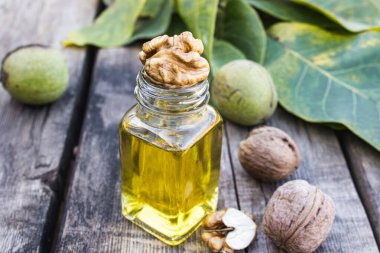 Ceviz ağacının yanında cam bir kavanozda ceviz yağı ve ahşap bir masada yeşil yapraklar..