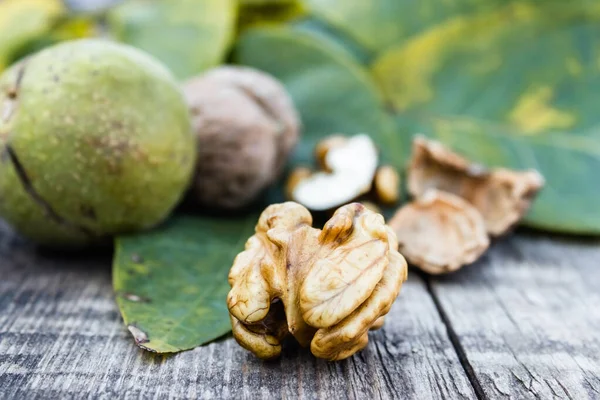 Núcleos de nueces y nueces enteras se encuentran junto a las nueces en cáscaras verdes y hojas verdes en una mesa de madera vieja rústica . —  Fotos de Stock