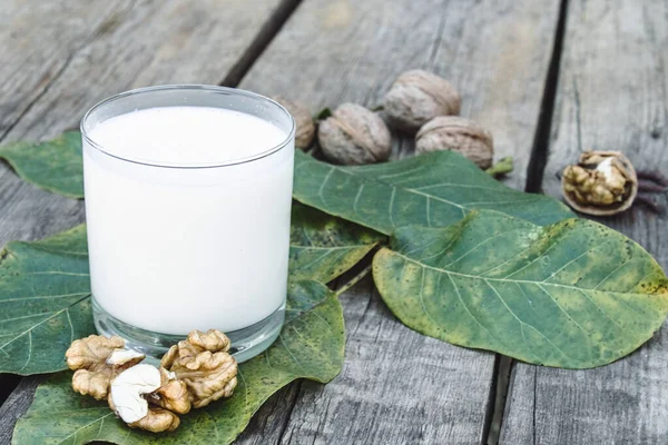 Eski ahşap bir masada ceviz yakınında bir bardakta vejetaryen fındık sütü. Cevizden vejetaryen sütü. Çevre yiyecekleri. — Stok fotoğraf
