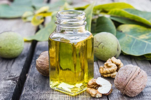 Walnut oil in a glass jar near walnuts and green leaves on a wooden table. — Stockfoto