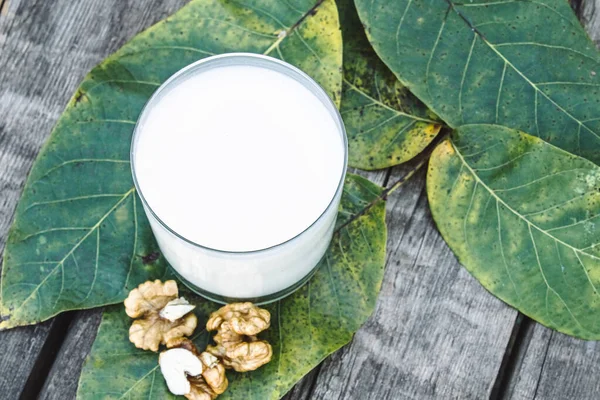 Eski ahşap bir masada bir bardak beyaz süt ve ceviz. Cevizden vejetaryen sütü. Çevre yiyecekleri. — Stok fotoğraf